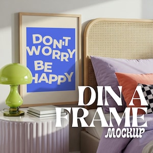 May include: A framed poster with a blue background and white text that reads "Don't Worry Be Happy" hanging on a wall above a bed with a light purple headboard and bedding. The bed has a pink nightstand with a green lamp and two books on top.