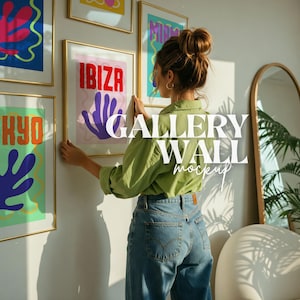 May include: A gallery wall mockup featuring a woman hanging a framed print with the word "IBIZA" in bold, white letters. The print has a purple hand design and a pink background. The other frames feature abstract designs in bright colours.