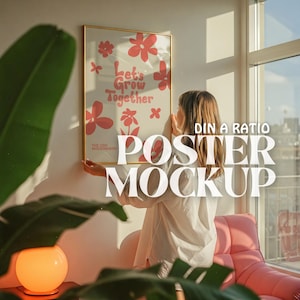 以下が含まれることがあります： 女性が壁にポスターを掛けています。ポスターは白地にピンクの花と「Let's Grow Together」の文字が書かれています。ポスターは金色の額縁に入っています。「DIN A RATIO POSTER MOCKUP」の文字がピンクの背景に白い文字で書かれています。