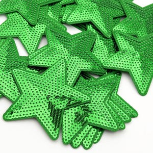 Pode incluir: Um monte de patches em forma de estrela de lantejoulas verdes. As estrelas têm aproximadamente 5 cm de diâmetro e são feitas de lantejoulas verdes brilhantes.