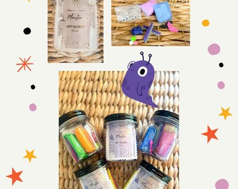 Może przedstawiać: Sześć szklanych słoików z czarnymi pokrywkami wypełnionymi kolorową plasteliną i ozdobionych etykietą z napisem "Monster Happy Halloween Slime". Słoiki znajdują się na plecionym wiklinowym podłożu. W tle znajdują się również kreskówkowe potwory i gwiazdki.