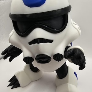 May include: White and black action figure with a blue helmet and black claws. The figure is in a standing pose with its arms outstretched.