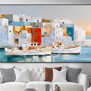 May include: A large rectangular oil painting featuring a coastal scene with two white fishing boats floating on blue water in front of a cluster of white, red, and gold buildings. The artwork uses thick, textured brushstrokes to depict the architecture.