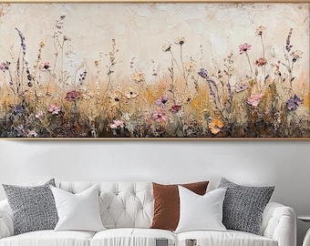 Op de afbeelding: Een rechthoekig, ingelijst schilderij toont een veld met wilde bloemen in roze, paarse, gele en bruine tinten. Het kunstwerk heeft een textuur, impasto-stijl, met zichtbare penseelstreken. De achtergrond is neutraal beige en de lijst is goudkleurig.