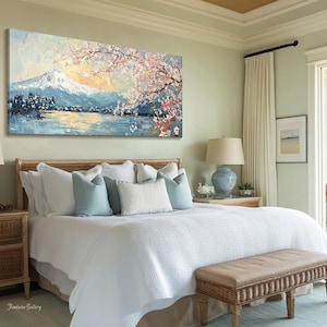 May include: A white bed with a light blue and white patterned headboard and a white duvet cover. The bed is decorated with blue and white throw pillows. A painting of a mountain scene with cherry blossoms hangs above the bed. A wicker end table with a lamp sits next to the bed. A wicker bench sits at the foot of the bed.