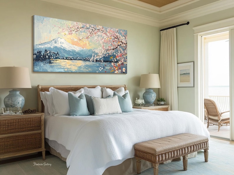 May include: A white bed with a light blue and white patterned headboard and a white duvet cover. The bed is decorated with blue and white throw pillows. A painting of a mountain scene with cherry blossoms hangs above the bed. A wicker end table with a lamp sits next to the bed. A wicker bench sits at the foot of the bed.
