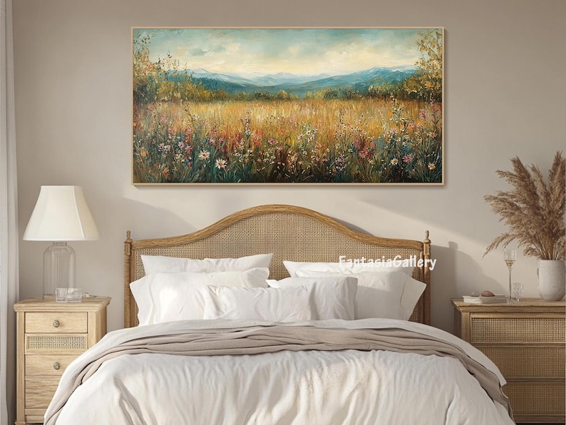 May include: A painting of a field of wildflowers with a mountain range in the background. The painting is framed and hanging on a wall above a bed with white linens.