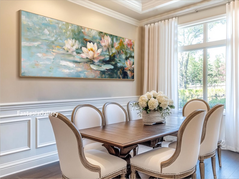 May include: A painting of white water lilies in a pond with a blue and green background. The painting is hanging on a wall in a dining room with a wooden table and white chairs.