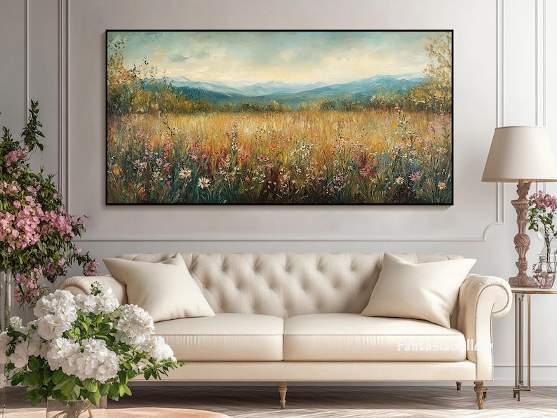 May include: A painting of a field of wildflowers in a meadow with a mountain range in the background. The sky is blue and there are clouds in the sky. The painting is framed in a black frame.