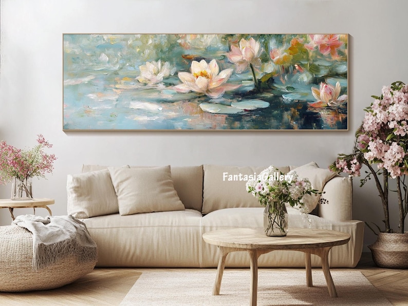 May include: A painting of white water lilies with pink accents on a blue and green background. The painting is framed and hanging on a white wall above a beige couch.