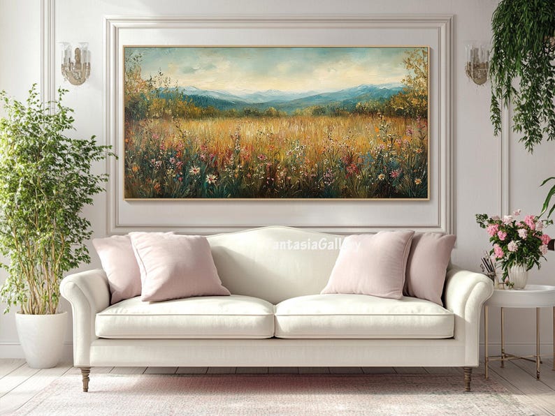 May include: A white sofa with two pink throw pillows in front of a painting of a field of wildflowers and a mountain range in the background.