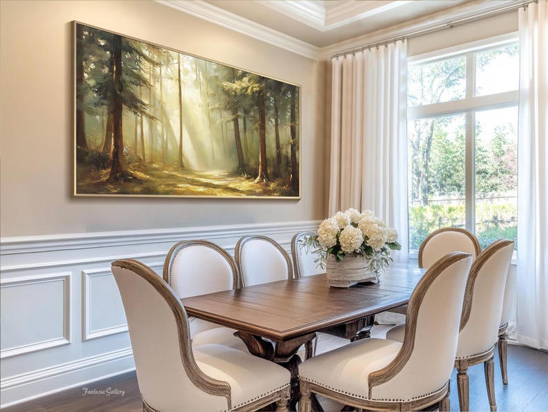 May include: A dining room with a large framed painting of a forest scene above a wooden table with six white upholstered chairs. The table is set with a vase of white flowers.