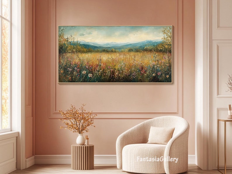 May include: A painting of a field of wildflowers with a mountain range in the background. The painting is in a gold frame and is hanging on a pink wall.