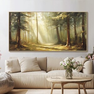 May include: A painting of a forest scene with sunlight streaming through the trees. The painting is in a gold frame and is hanging on a wall above a white couch.