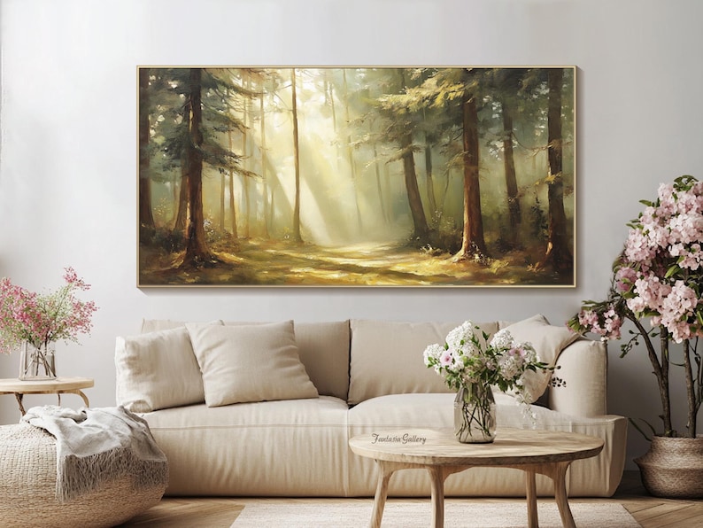 May include: A painting of a forest scene with sunlight streaming through the trees. The painting is in a gold frame and is hanging on a wall above a white couch.