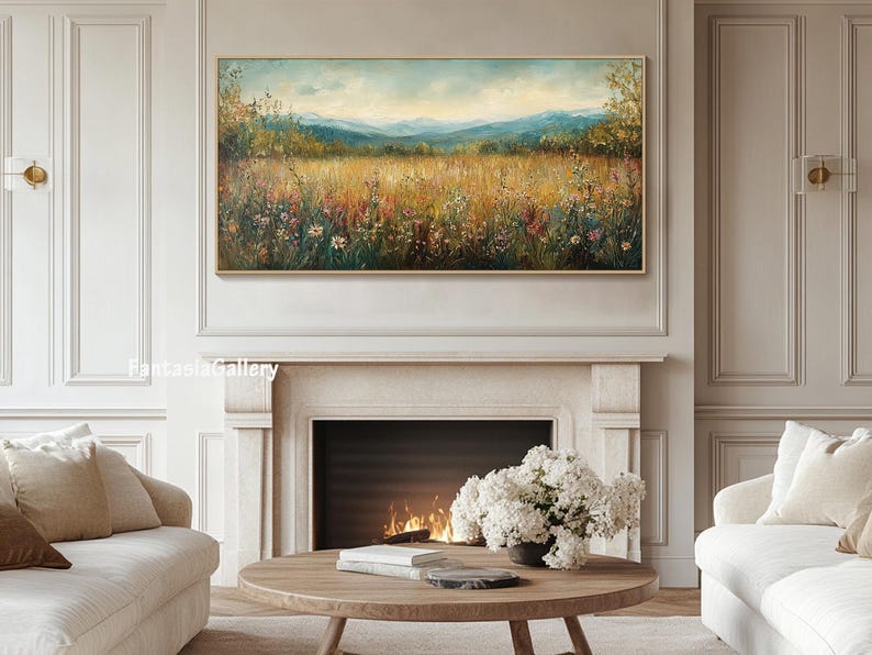 May include: A painting of a field of wildflowers with a mountain range in the background. The painting is in a gold frame and is hanging on a wall above a fireplace.