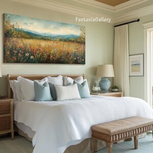 May include: A white bed with a light blue and white patterned headboard and a white duvet cover. The bed is in a bedroom with a large painting of a field of wildflowers hanging above the headboard. There is a wicker nightstand next to the bed and a wicker bench at the foot of the bed.