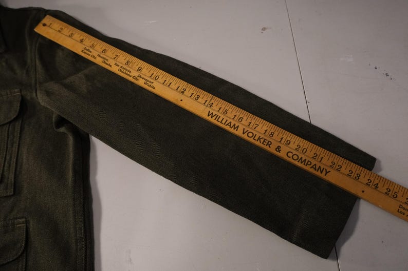 Puede incluir: Manga de chaqueta verde oscuro con dos bolsillos y una regla de madera que mide hasta 63.5 cm. La regla est&aacute; marcada con el texto "WILLIAM VOLKER & COMPANY".