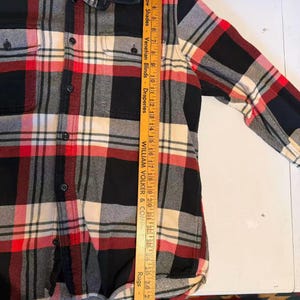 以下が含まれることがあります： 黒、赤、クリーム色のクラシックなチェック柄の長袖ボタンダウンフランネルシャツ。 シャツには胸ポケットが2つと襟が付いています。 ブランド名「FILSON」が確認できます。 シャツの長さは約74cmです。