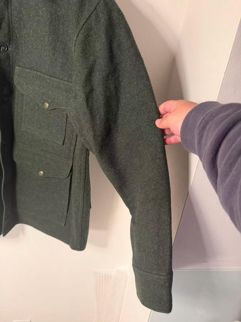 May include: Dark green wool jacket with two chest pockets and button closures. The jacket has a classic design with a tailored fit. The sleeves are long with buttoned cuffs. The jacket is made of a thick, warm material.