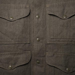 Puede incluir: Primer plano de una camisa abotonada marr&oacute;n con cuatro bolsillos delanteros y cuello puntiagudo. La camisa tiene una tela texturizada y varios botones redondos en el centro. Los bolsillos tienen esquinas redondeadas y est&aacute;n asegurados con peque&ntilde;os botones.