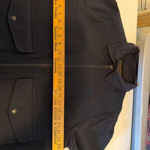 Puede incluir: Una chaqueta azul marino con cierre de cremallera completo y dos bolsillos delanteros con cierre de bot&oacute;n. La chaqueta tiene cuello y la marca "FILSON" es visible en la etiqueta. La chaqueta mide unos 66 cm de largo.