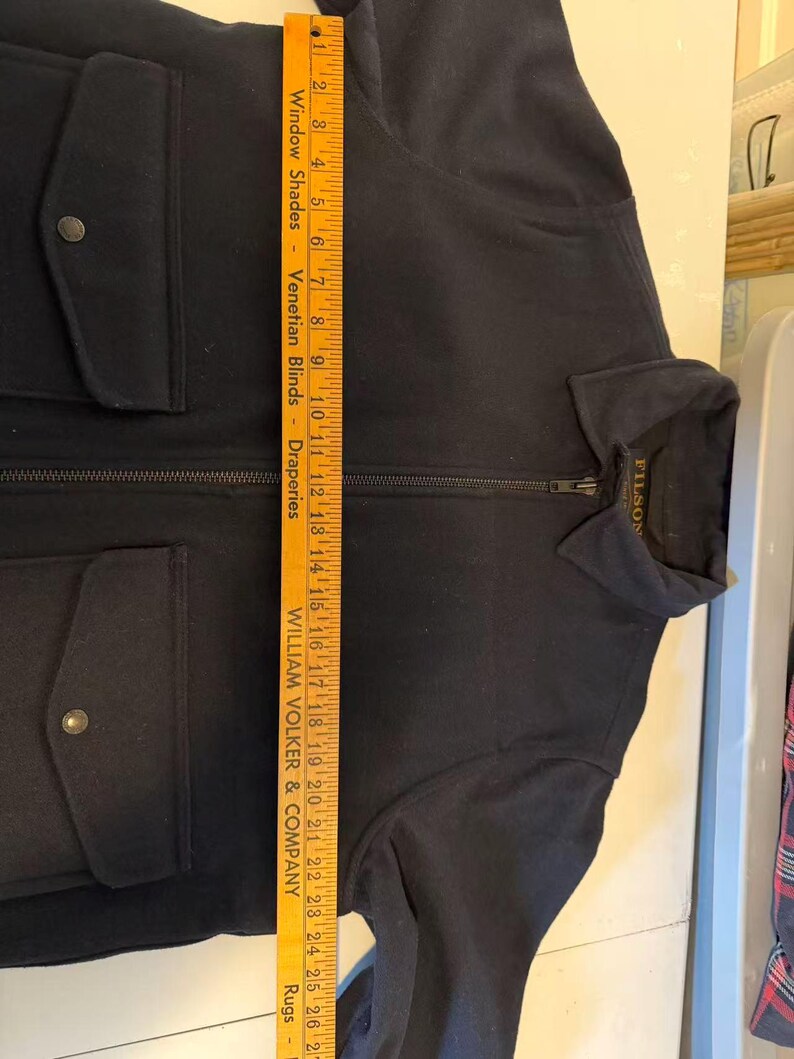 Puede incluir: Una chaqueta azul marino con cierre de cremallera completo y dos bolsillos delanteros con cierre de bot&oacute;n. La chaqueta tiene cuello y la marca "FILSON" es visible en la etiqueta. La chaqueta mide unos 66 cm de largo.