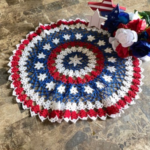 May include: A crocheted doily with red, white, and blue stars. The doily is made with a delicate crochet stitch and has a scalloped edge.
