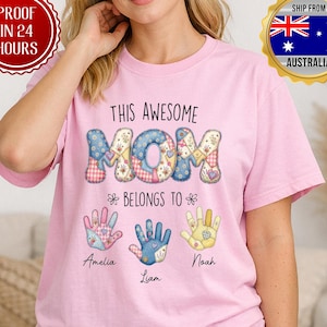 May include: A pink t-shirt featuring the text "THIS AWESOME MOM" in a patchwork design. Below the text are three handprints with the names Amelia, Liam, and Noah. A red circular badge reads "PROOF IN 24 HOURS".