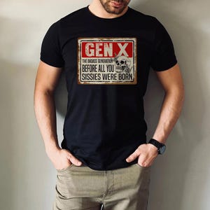 May include: A black t-shirt with a red and white sign that says "Gen X The Badass Generation Before All You Sissies Were Born". The sign has a skull with a bone in its mouth and a middle finger.