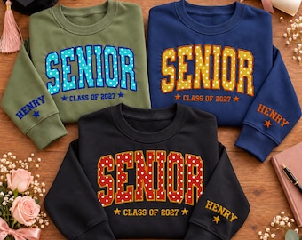 May include: Three crewneck sweatshirts in olive green, navy blue, and black. Each features the word SENIOR in polka-dot lettering, the text CLASS OF 2027, and the name HENRY embroidered on the sleeve with a star icon.