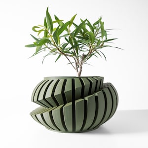 May include: A green ceramic planter with a unique geometric design. The planter is made up of multiple overlapping, vertical, rectangular shapes. A small green plant is growing inside the planter.
