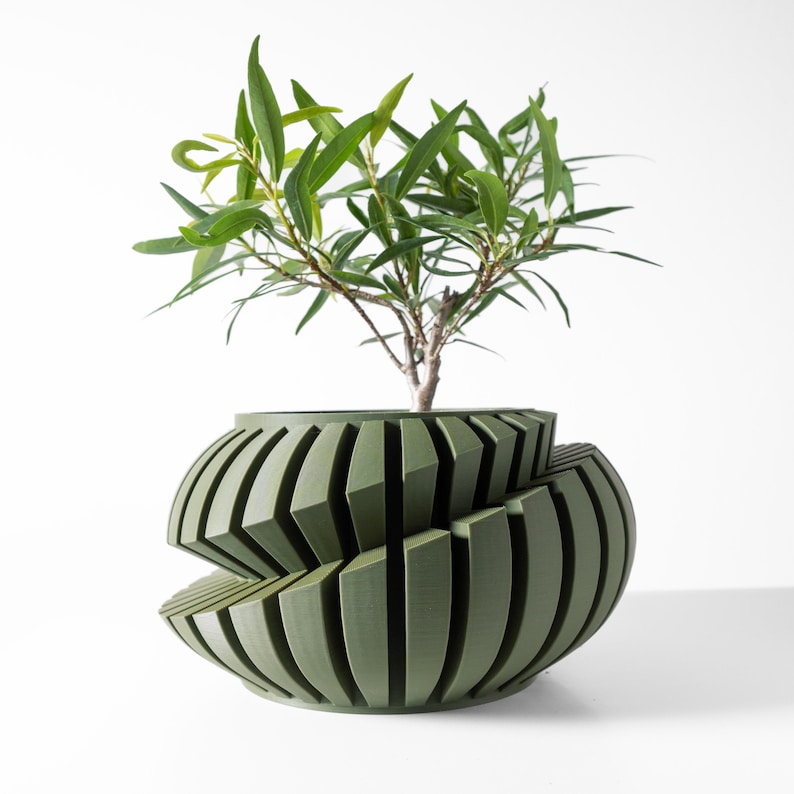 May include: A green ceramic planter with a unique geometric design. The planter is made up of multiple overlapping, vertical, rectangular shapes. A small green plant is growing inside the planter.