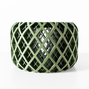 May include: A cylindrical olive green planter featuring a complex, three-dimensional lattice structure. The exterior is composed of intersecting diamond-shaped patterns that create a hollow, open-work design, revealing a dark interior core.