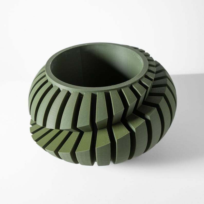 May include: A green ceramic planter with a unique, geometric design. The planter has a wide, round opening and a series of vertical ridges that create a textured surface.
