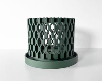 May include: A dark green cylindrical planter featuring a repeating geometric honeycomb lattice pattern throughout its exterior walls. The planter sits securely on a matching circular drip tray with a flat base and a slightly raised outer rim edge.