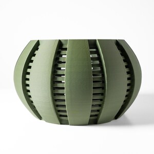 May include: A sage green planter with a rounded, bulbous shape featuring vertical slats that create a cage-like appearance. The design consists of wide, solid vertical bands alternating with narrow, recessed horizontal bars throughout the structure.