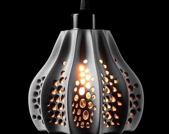 May include: A dark gray pendant light with a fluted, bell-shaped shade featuring a pattern of irregular, circular cutouts. Warm light glows through the perforations, contrasting with the dark, textured surface of the fixture against a black background.