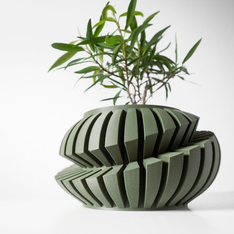 May include: A green, geometric planter with a unique, layered design. The planter is made of a smooth, textured material and features a series of overlapping, curved panels. A small green plant is growing inside the planter.