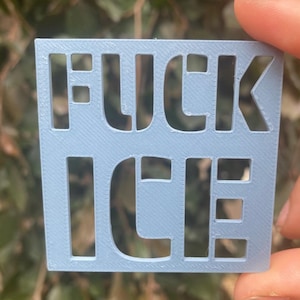 Könnte beinhalten: Ein hellblaues Quadrat mit den Worten "FUCK ICE" ausgeschnitten. Die Buchstaben sind in einer serifenlosen Schriftart. Das Objekt wird von den Fingern einer Person gehalten.