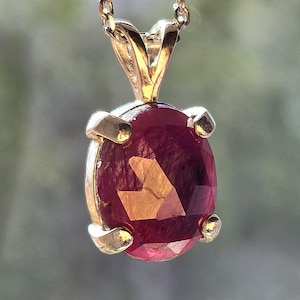 May include: A gold chain necklace with a pendant featuring a large, oval-shaped ruby gemstone.