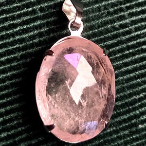 Op de afbeelding: Ovale hanger met een lichtroze, gefacetteerde edelsteen. De edelsteen is gezet in een zilverkleurig metalen frame met een bijpassende balein voor een ketting. De hanger heeft een geometrisch ontwerp.