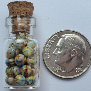 May include: A small clear glass bottle with a cork stopper filled with miniature multi-colored swirl glass marbles. A 1996 United States dime is placed next to the bottle to provide a clear sense of scale for the tiny glass spheres inside.
