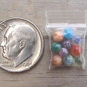 May include: A small plastic bag filled with colorful glass marbles. The marbles are various shades of blue, green, red, and yellow. The bag is about the size of a US dime.