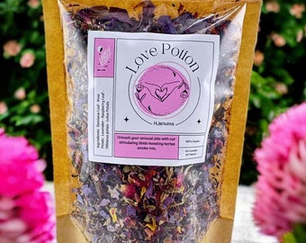 May include: A brown paper pouch with a clear plastic window, containing a blend of dried herbs and flowers. The pouch has a label that reads "Love Potion" and "Hanuma". The label also states that the product is 100% organic and contains no additives.