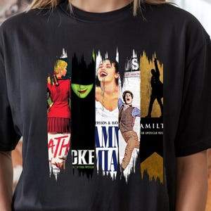 May include: Black t-shirt featuring a collage of musical theater posters. The design includes images and text from popular Broadway shows such as "Wicked," "Mamma Mia," and "Hamilton." The shirt is a crew neck and has short sleeves.