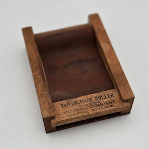 May include: A wooden roller with a metal roller inside. The roller is labeled "Tailor-Made Roller" with the company name "Hollisg Company, Van Dyne, Wisconsin".