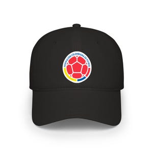 May include: A black baseball cap featuring a circular logo on the front. The logo displays a red soccer ball graphic surrounded by the text FEDERACIÓN COLOMBIANA DE FÚTBOL, with yellow and blue curved segments at the bottom of the circle.