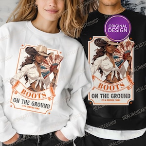 Puede incluir: Sudaderas blancas y negras con un diseño gráfico. El diseño incluye una ilustración de vaquera con un abanico, un sombrero de vaquero y el texto "BOOTS ON THE GROUND". Las sudaderas son de estilo casual.