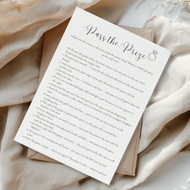 May include: A wedding game card titled "Pass the Prize" with elegant script. The card features a ring graphic and instructions for a bridal shower game. The card is on a neutral background, suggesting a classic, understated aesthetic.